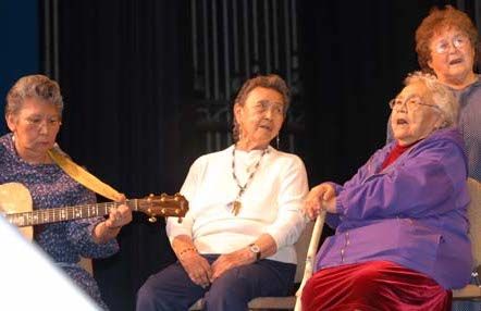 A woman plays the guitar while three other women sing.