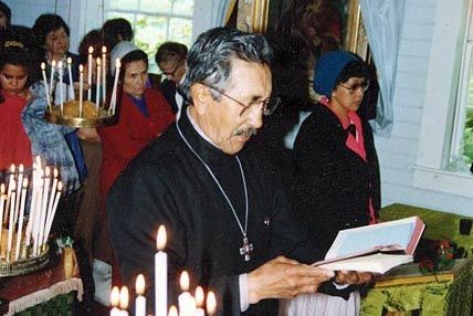 A priest with an open hymnal surrounded by standing people at a church service.