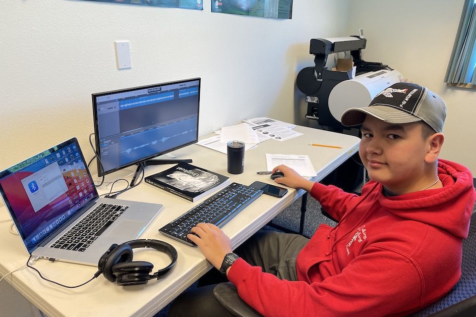 Young man sitting in front of a computer with a microphone.